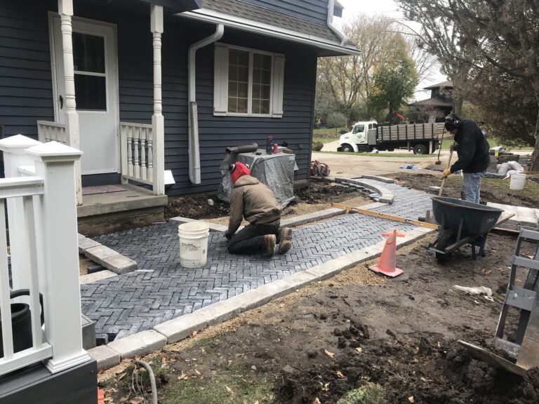 Workers installing pavers outside blue house.